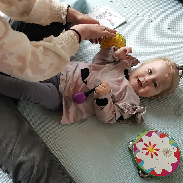 Lächelndes Kleinkind liegt auf dem Boden und spielt in einer Eltern-Kind-Gruppe.