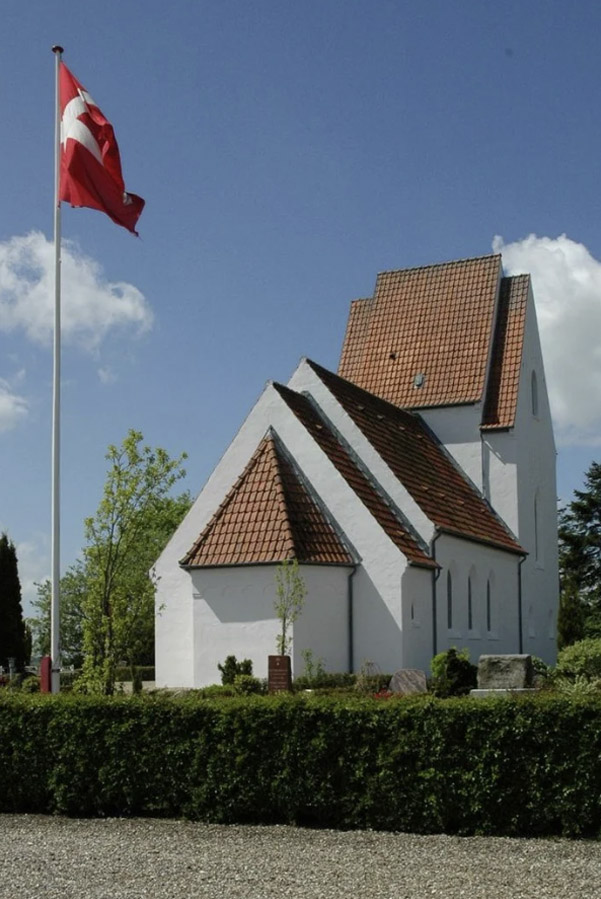 En hvid kirke med rødt tegltag ved siden af en flagstang med det danske flag.