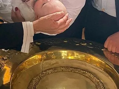 Et spædbarn holdes over en gylden døbefont.