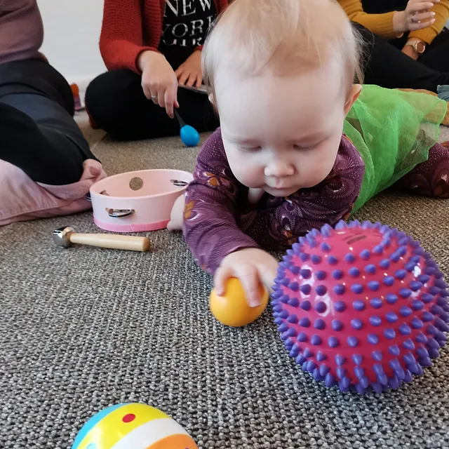 Baby auf dem Boden spielt mit bunten Bällen und Musikinstrumenten.