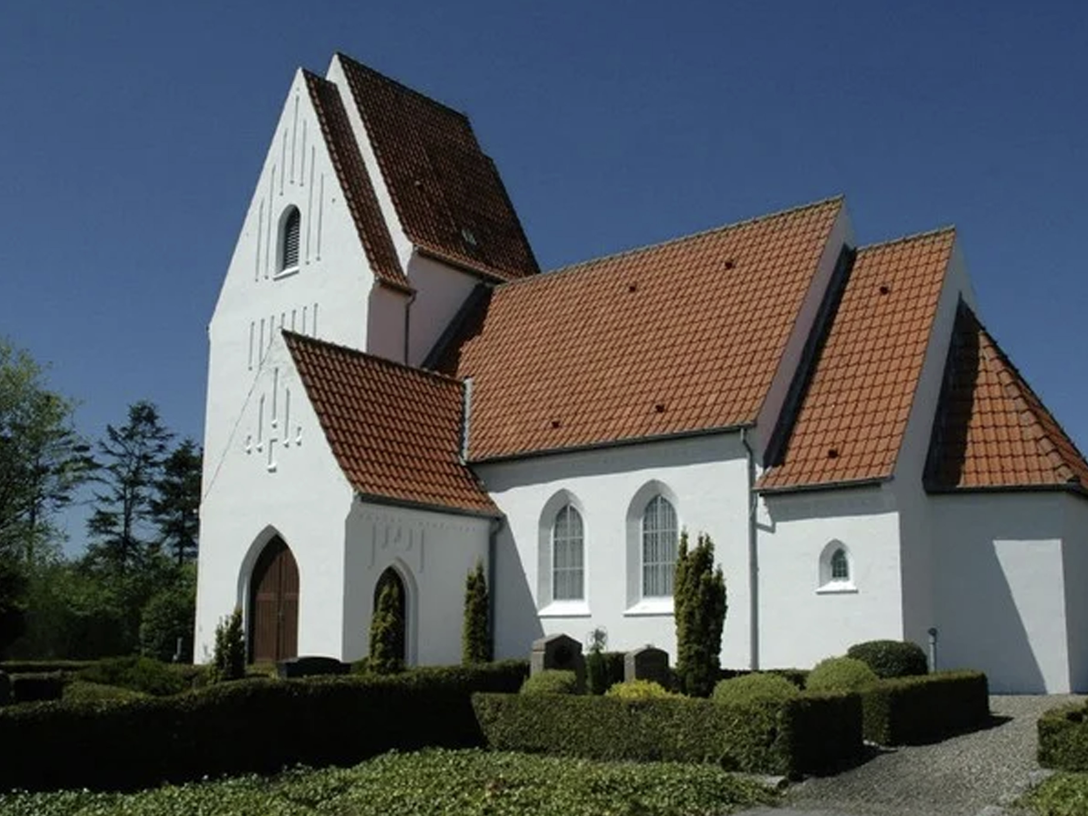 Hvidlimet kirke med rødt tegltag og tilhørende kirkegårdshave.