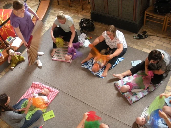 Draufsicht auf Erwachsene und Babys, die sich im Kreis auf Matten versammelt haben.